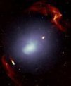 Autor: Francesco de Gasperin, SARAO - Velmi hmotná kupa galaxií Abell 3667. Jednotlivé galaxie jsou příliš malé na to, abychom je mohli rozlišit. Bílé mlhavé zbarvení ukazuje rozložení plynu, který prostupuje prostorem mezi galaxiemi této kupy galaxií. Červeně zbarvené struktury představují dvě velké rázové vlny, které byly generovány v průběhu vzniku kupy galaxií.