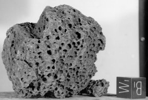 Astronautům se na povrchu Měsíce podařilo získat řadu horninových vzorků dokládajících vysokou pórovitost měsíčních sopečných hornin, a tedy doložit přítomnost sopečných plynů v magmatu. Na snímku se nachází vzorek 15556  získaný posádkou Apolla 15, který reprezentuje materiál tvořící měsíční moře. Kostka v pravém dolním rohu má velikost hrany 1 palec (2,54 cm). Autor: Apollo 15, NASA, volné dílo.