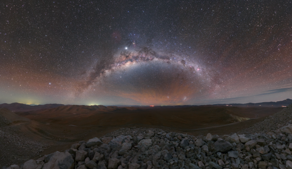 Oblouk Mléčné dráhy a výrazné červené airglow ve směru na východ od Cerro Armazones. Kameny v dolní části snímku vznikly po odstřelení vrcholu v roce 2014. V krajině pouště také uvidíte stín samotné hory (na úrovni pod centrem Mléčné dráhy), neboť v době focení ještě do zad slabě svítil Měsíc. Autor: Petr Horálek/ESO.