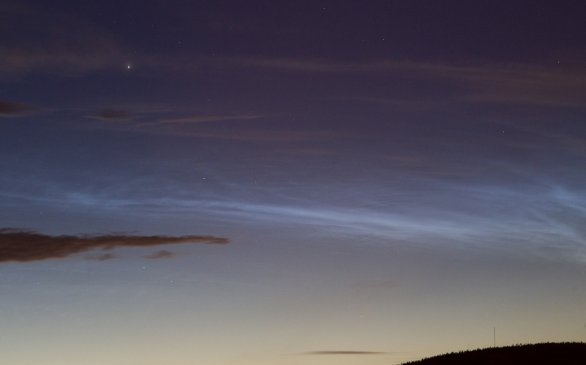 NLC, noční svítící oblaka, stříbromodrá struktura na pozadí blízkých tmavých oblak středních až vysokých pater. Fotografováno krátce po 23. hodině 6. června 2020. Jasná hvězda je Capella. Autor: Martin Gembec