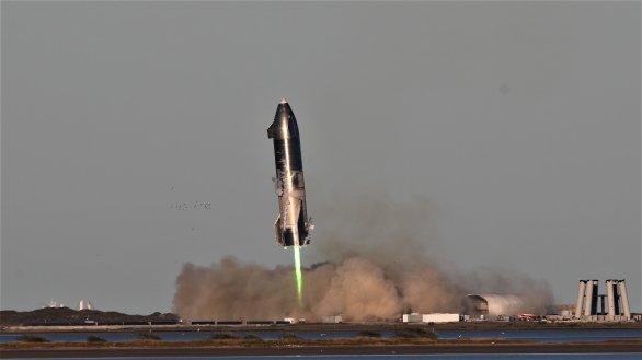 Starship SN8 těsně před dosednutím. Po úspěšném testu vidíme, že motory ztratily tah a pravděpodobnou absenci dostatku paliva naznačuje zelená barva plamene (kdy možná přebytek kyslíku ve spalovací komoře tavil měď v motoru). Autor: BocaChicaGal/NASASpaceflight.com