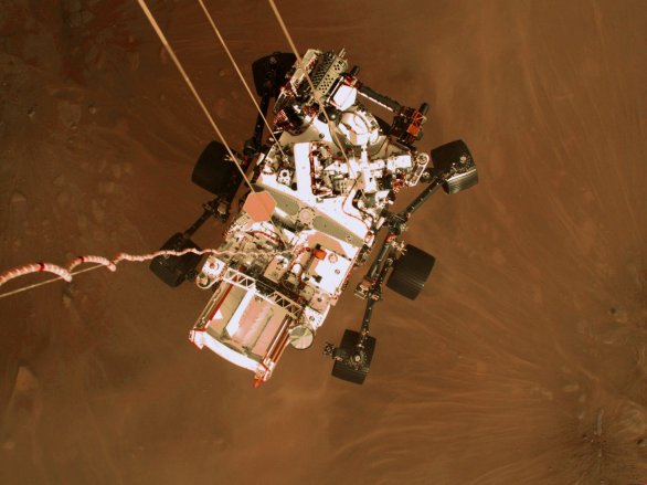 Pohled na vozítko Perseverance před dosednutím na povrch Marsu (kamera na sestupovém jeřábu, výška asi 2 metry nad povrchem) Autor: NASA/JPL-Caltech