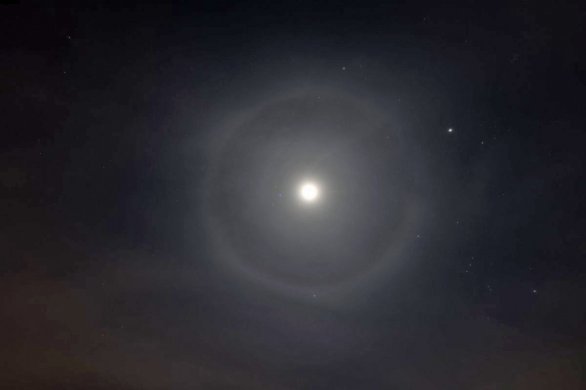 Malé halo kolem Měsíce 8. 3. 2025. Průměr tohoto kruhu je 44° Tento halový jev vzniká na ledových krystalcích vysokých oblak a možná pomohl i příliv saharského písku. Hned pod Měsícem byl Mars, vpravo je jasný Jupiter, nahoře mimo kruh Capella a dole se kruh dotýká Prokyona. Vpravo dole je Orion. Autor: Jakub Veselý, Sloupnice
