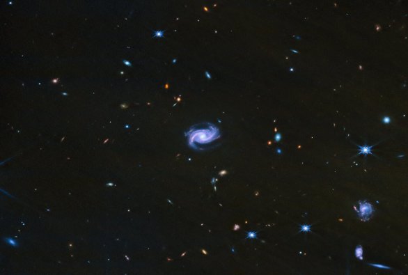 Spirální galaxie v pozadí mlhoviny IC 348 zachytil v infračerveném oboru spektra dalekohled JWST. Bližší spirální galaxie jsou miliony světlených roků od nás, zatímco ty malé vzdálené tečky bez tvaru jsou až miliardy světelných let vzdálené Autor: ESA/Webb, NASA, CSA, K. Luhman, C. Alves De Oliveira, M. Zamani (ESA/Webb)